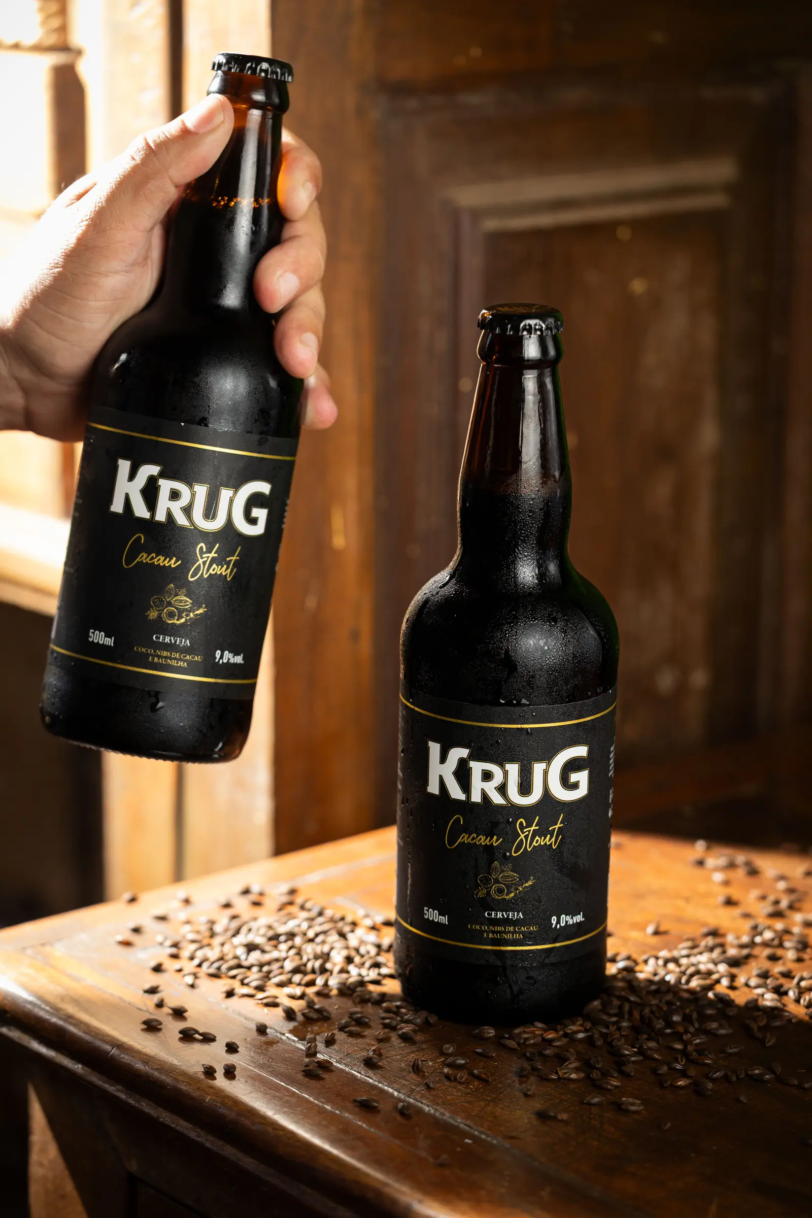 Duas garrafas de Krug Cacau Stout sobre mesa de madeira com maltes torrados